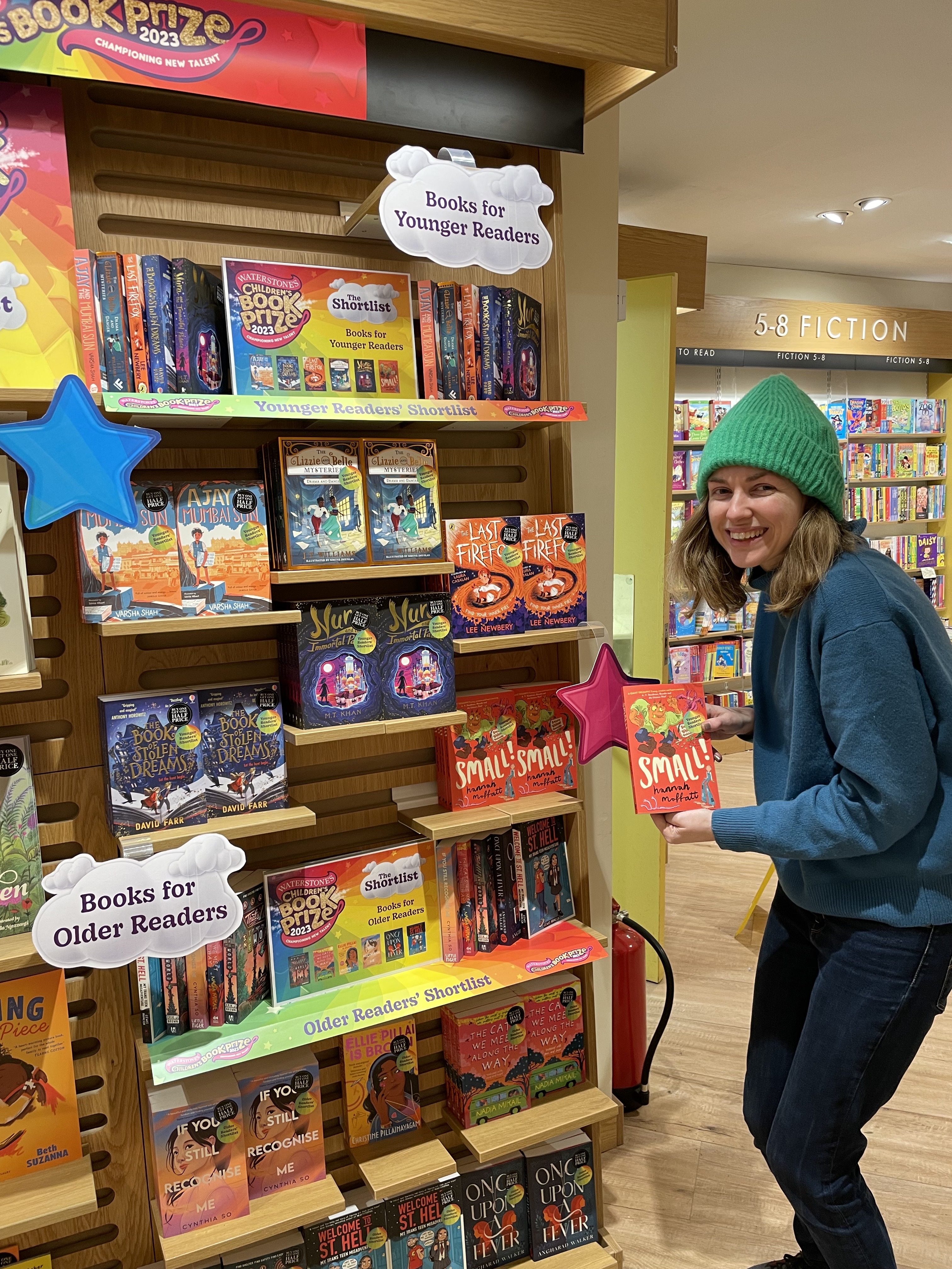 Me holding a copy of Small in front of a display of shortlisted books