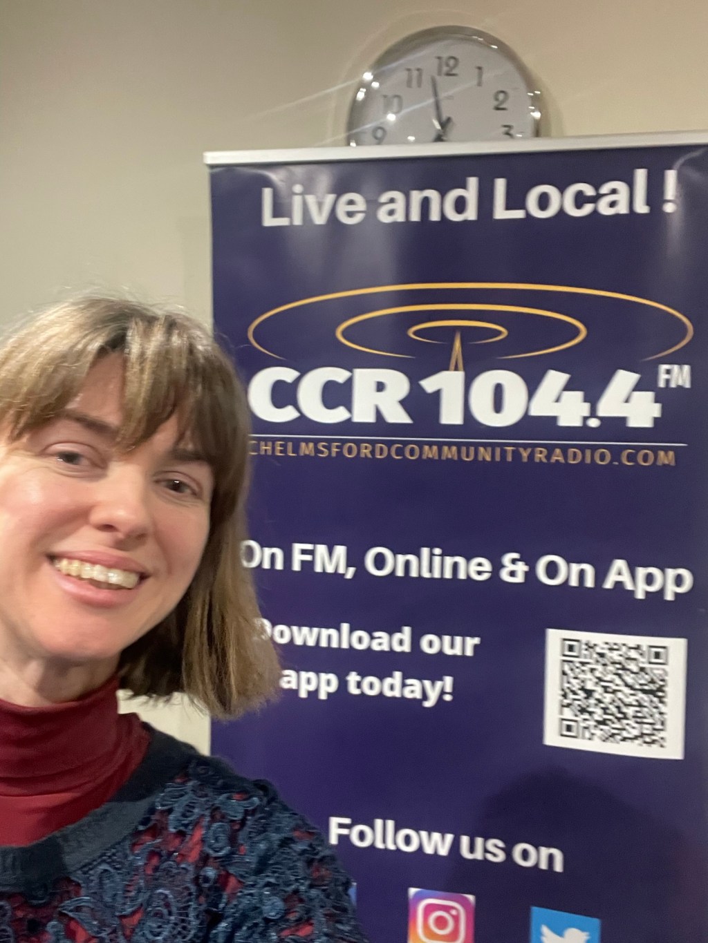 Me standing in front of a purple pull up banner that says 'Live and Local. CCR 104.4FM on FM, Online & On App. Download our app today!